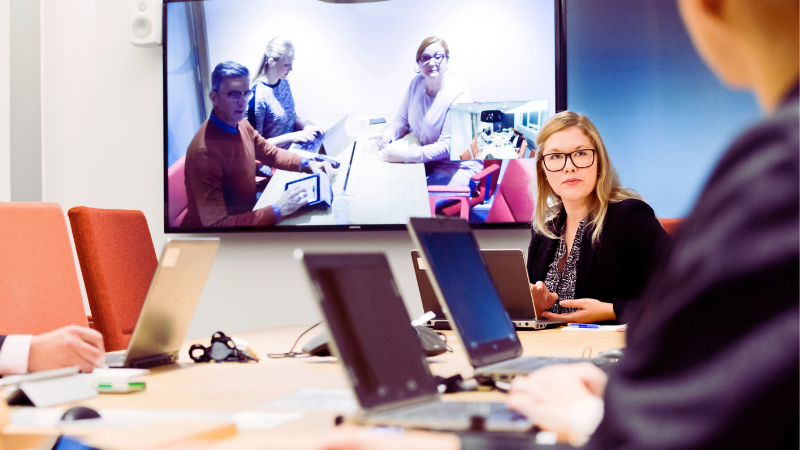 Experter på hybridmöten. Tre arbetstagare i förhandlingsrummet, tre arbetstagare deltar på distans. Alla lyssnar koncentrerat på en person utanför bilden.